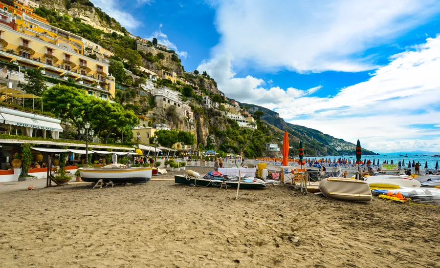 Boote auf dunklem Sand unter einer Stadt am Hang