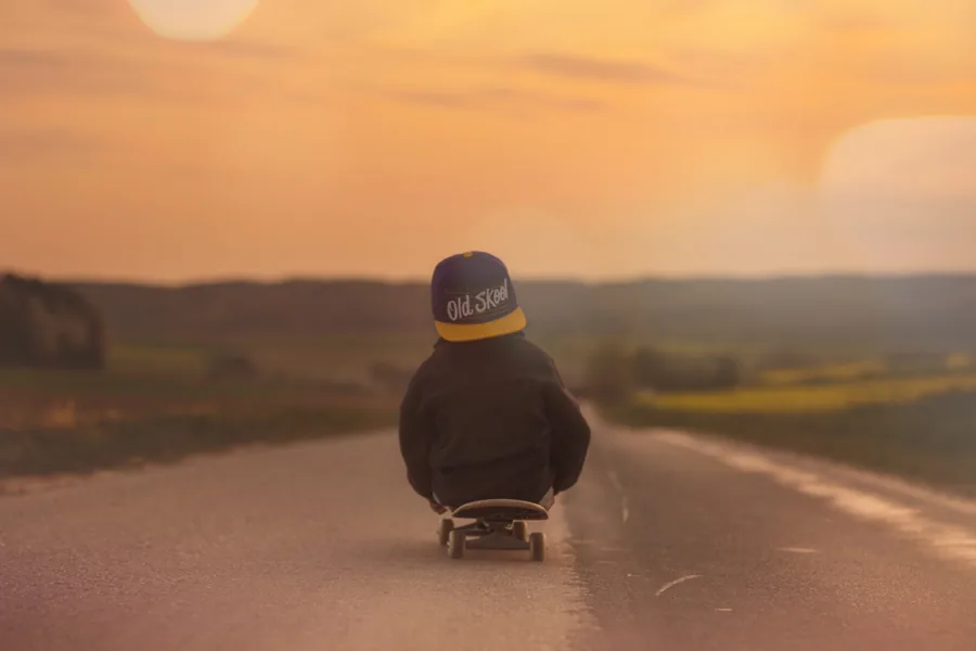 A Child Sitting on a Skateboard at Sunset