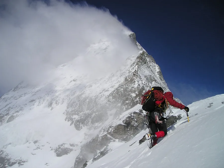 Ein Bergsteiger unter einem verwehten Schneegipfel